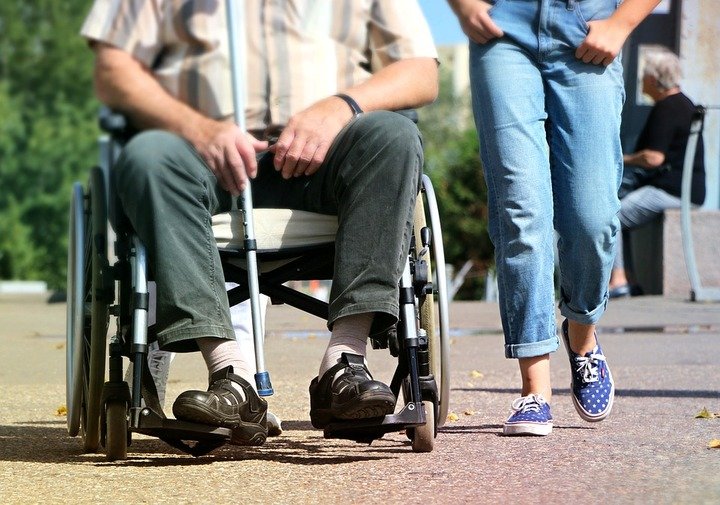 una persona en silla de ruedas y alguien caminando a su lado