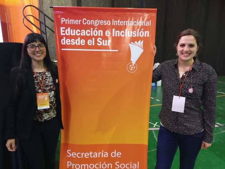 Foto de 2 miembros de la fundacion al lado de un banner del Primer Congreso Internacional Educación e Inclusión desde el Sur