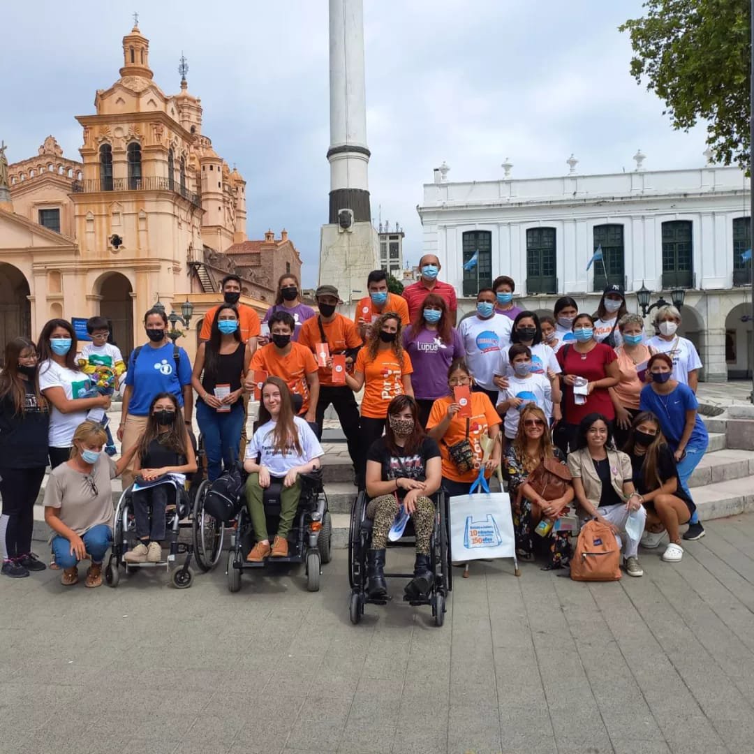 Grupo de fpersonas de diferentes organizaciones sociales y agrupaciones de EPOF sonríen frente a cámara (con barboijos) detras e ve la Catedral de Córdoba y el Cabildo
