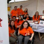 11 personas con las remeras naranjas de Por Igual Mas sonrien a la camara en el stand