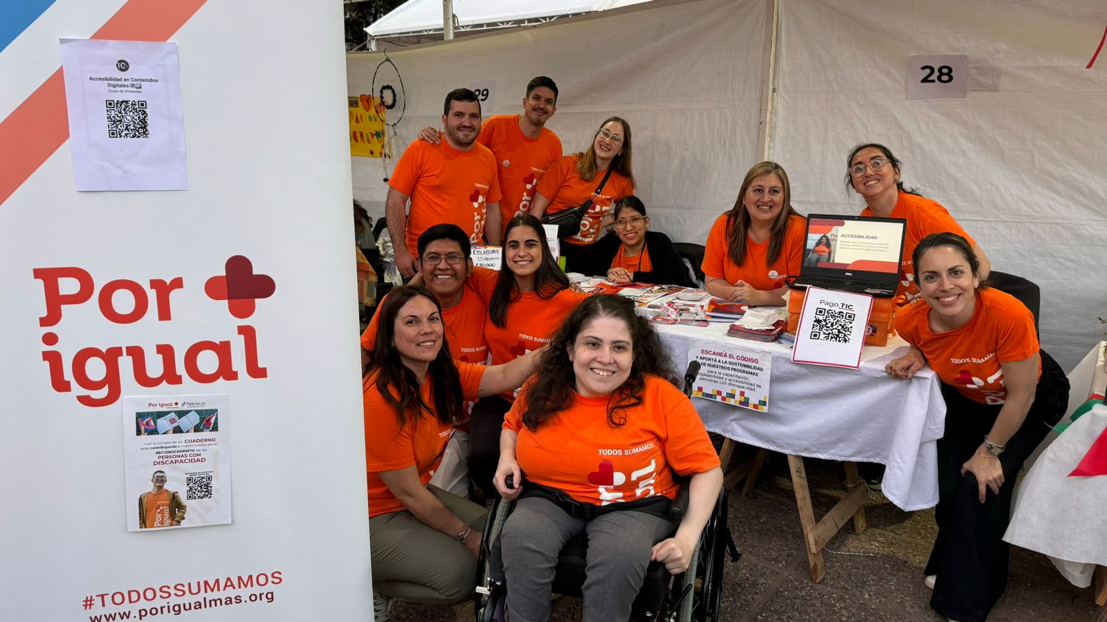 11 personas con las remeras naranjas de Por Igual Mas sonrien a la camara en el stand