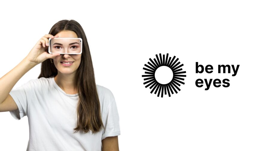 Imagen promocional con fondo blanco que muestra a la izquierda a una mujer sonriente con remera blanca sosteniendo un teléfono inteligente frente a sus ojos. En la pantalla del celular se observa una imagen de sus propios ojos. A la derecha aparece el logotipo en negro de la aplicación «be my eyes», junto al texto con el nombre de la plataforma