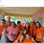 grupo de nueve personas, todas sonriendo y posando juntas de forma cercana y amistosa. La mayoría de ellas lleva camisetas de color naranja brillante con el logo de la Fundación Por Igual Más, que dice 'Por Igual Más'. El grupo incluye hombres y mujeres, algunos con distintas discapacidades, abrazándose o con los brazos sobre los hombros de los demás. Arriba, pequeño, se ve el logo Buscador Xinus en letras azules.