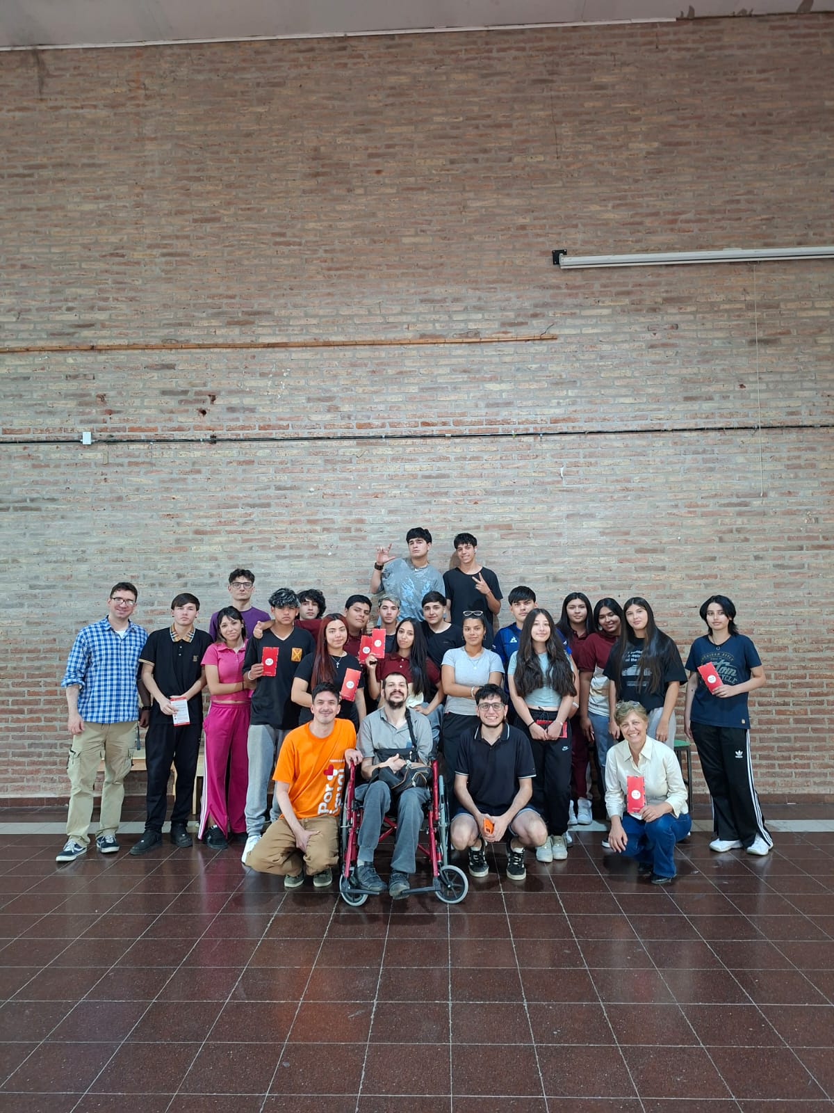 Grupo de personas ubicadas de frente, en su mayoría jóvenes, paradas y sentadas. Una de ellas en silla de ruedas.