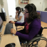 dos mujeres en sillas en rueda frente unas computadoras